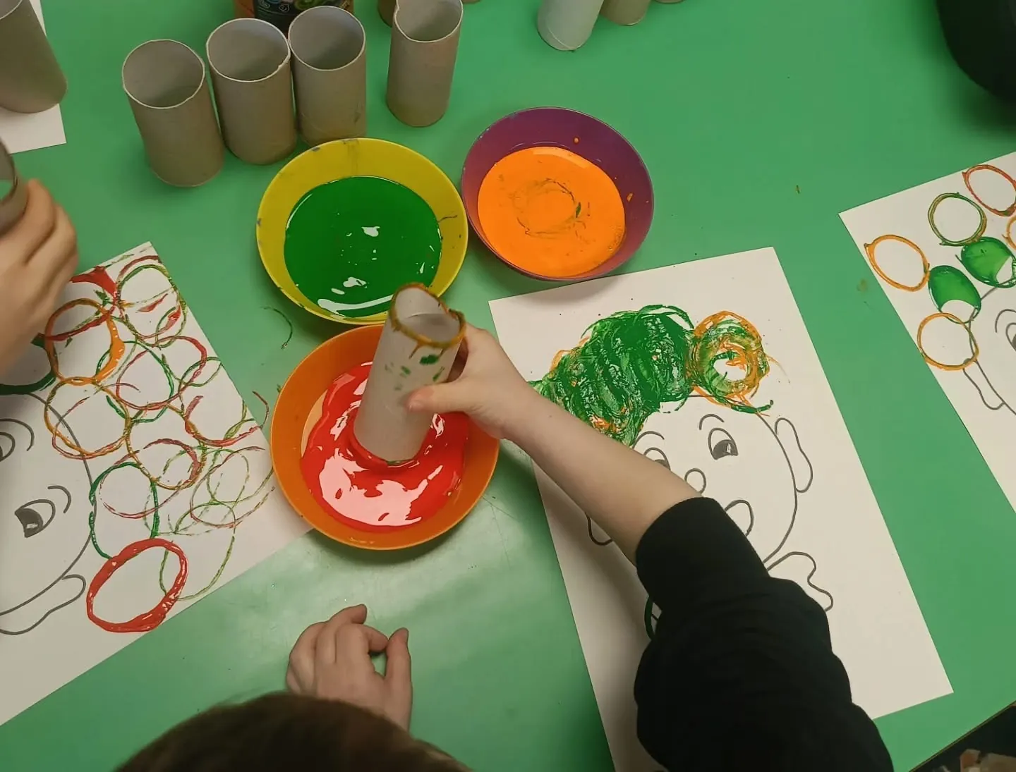 Bambini dipingono cerchi colorati usando rotoli di cartone e tempere