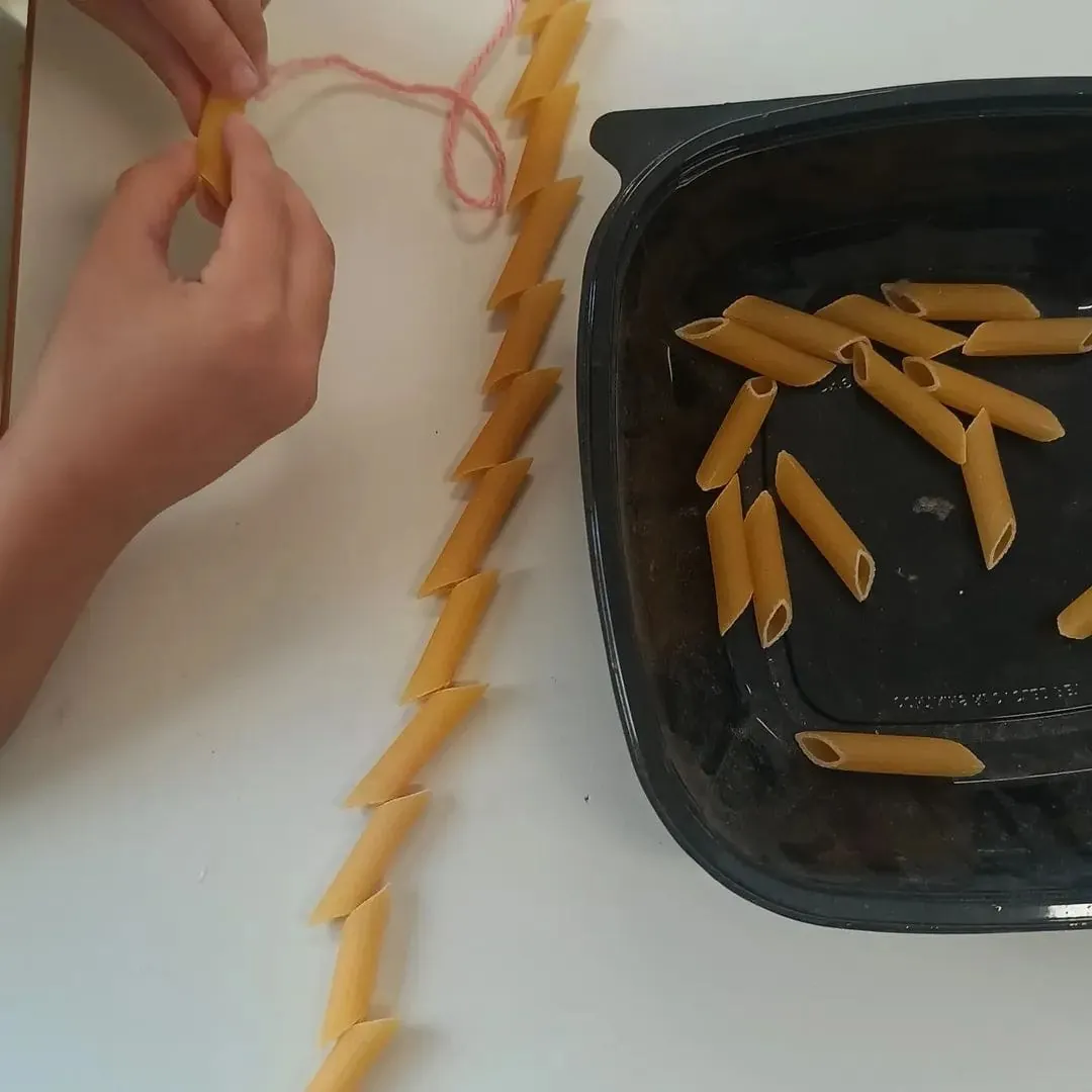 Un bambino infila le penne di pasta in un filo di lana nel laboratorio di motricità fine