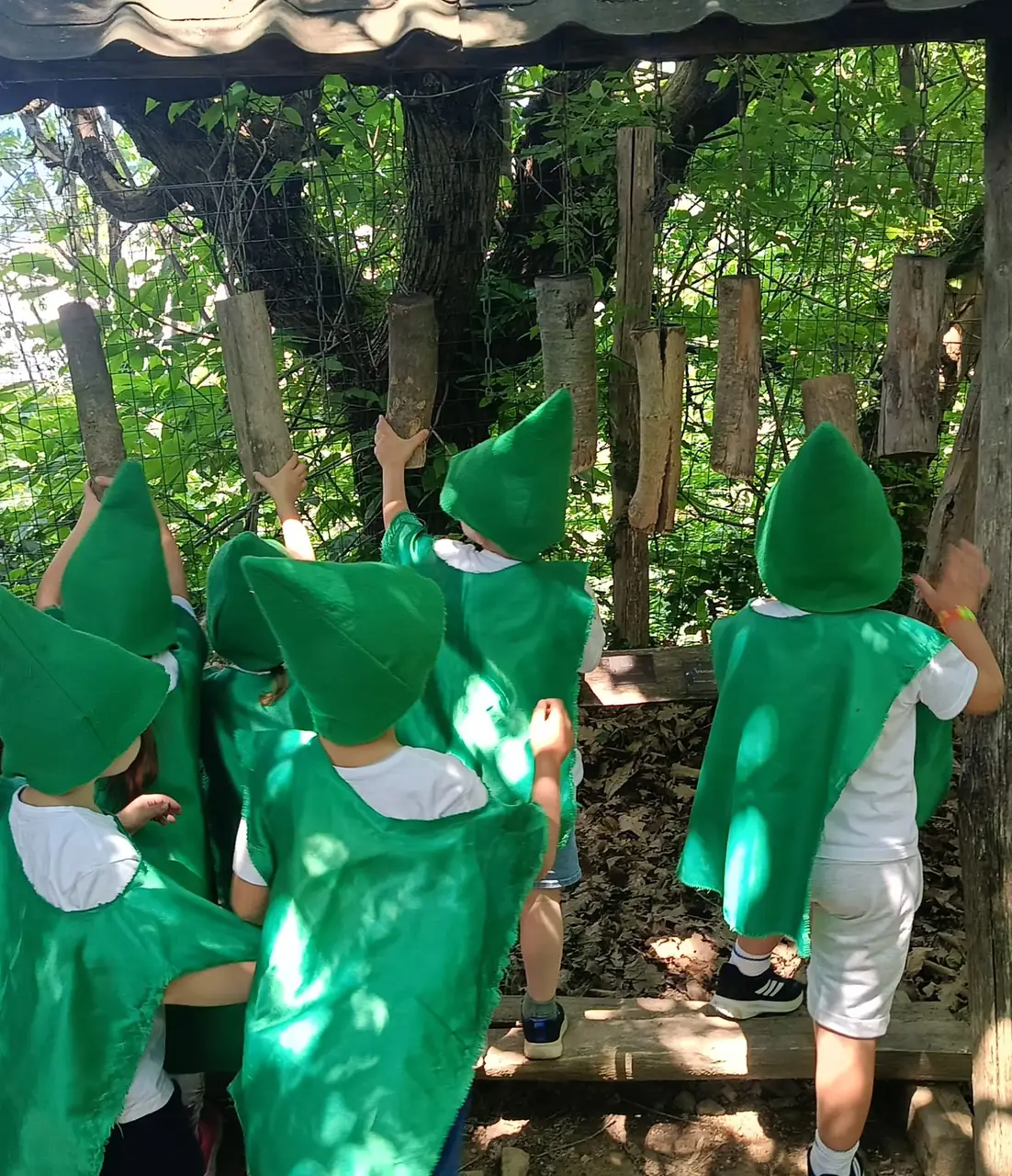 Bambini vestiti da folletti toccano i tronchi appesi di un percorso sensoriale nel bosco